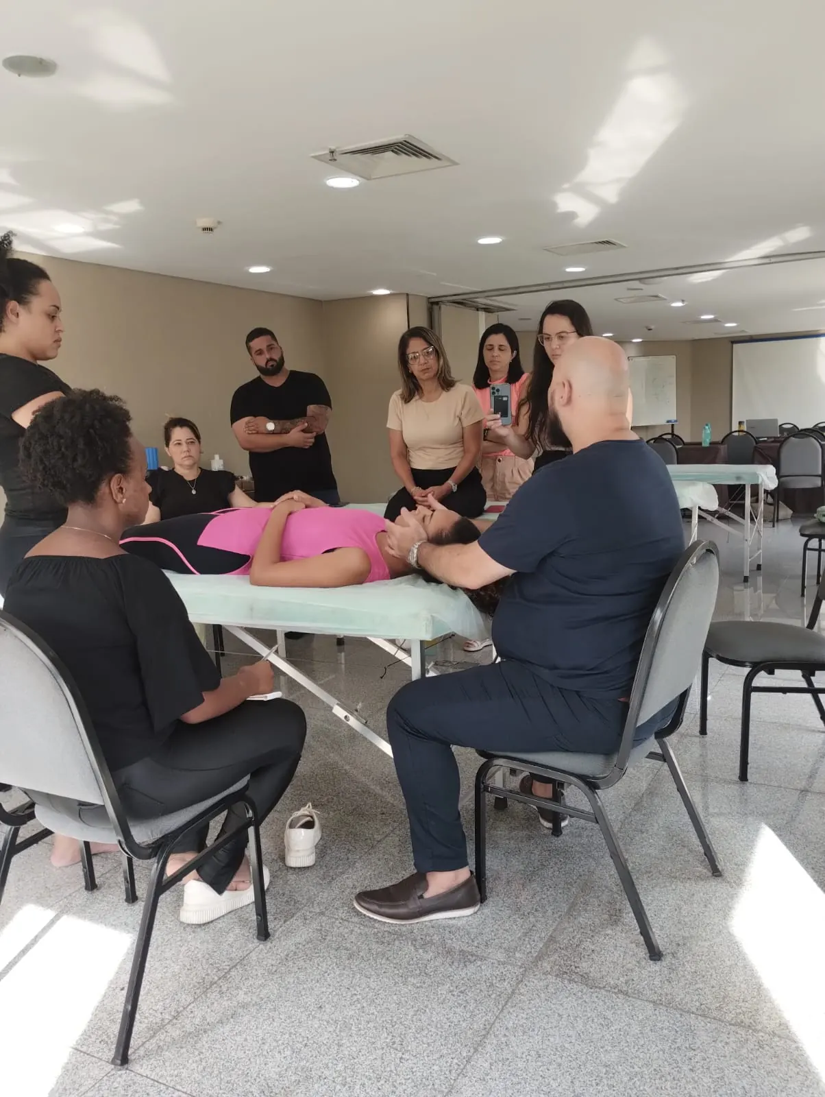 Turma reunida em volta da maca acompanhando demonstração de avaliação do paciente